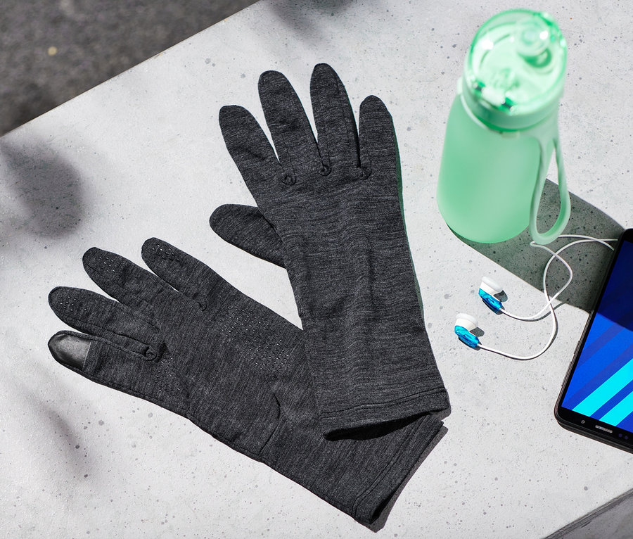 Auf einer grauen Oberfläche liegen Handschuhe mit Merinowolle, eine Wasserflasche, Kopfhörer und ein Handy.