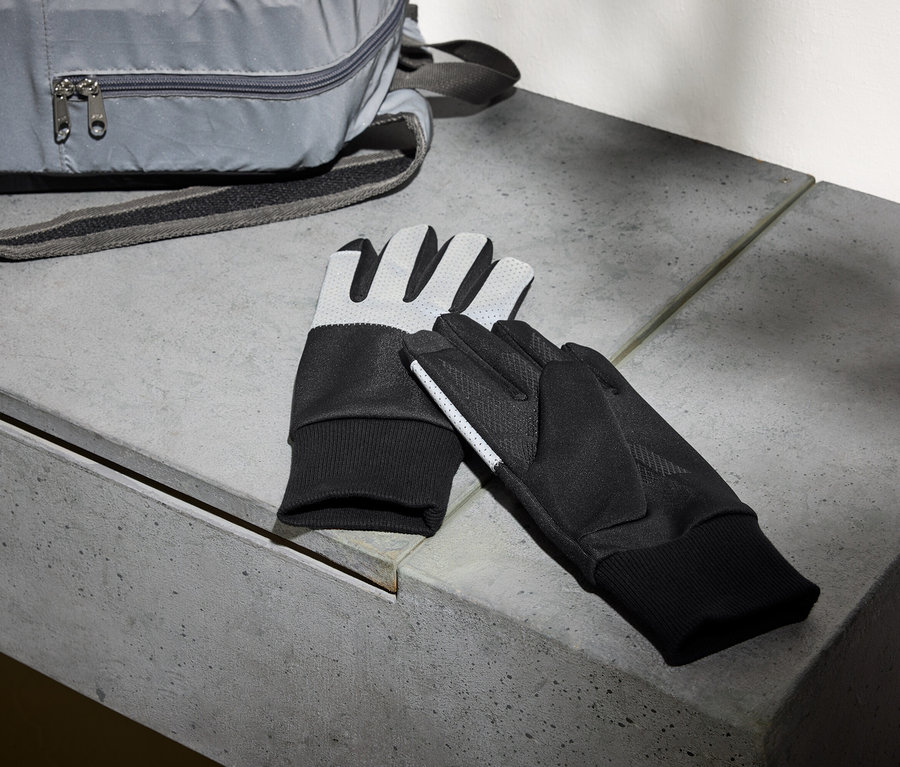 Ein grauer Rucksack und ein Paar schwarze Handschuhe liegen auf einer Betonbank.