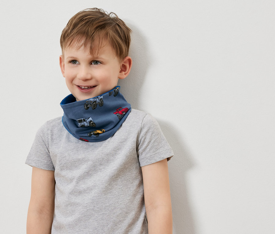 Lächelnder Junge trägt ein blaues Schlauchtuch mit Autoaufdruck und ein graues T-Shirt.