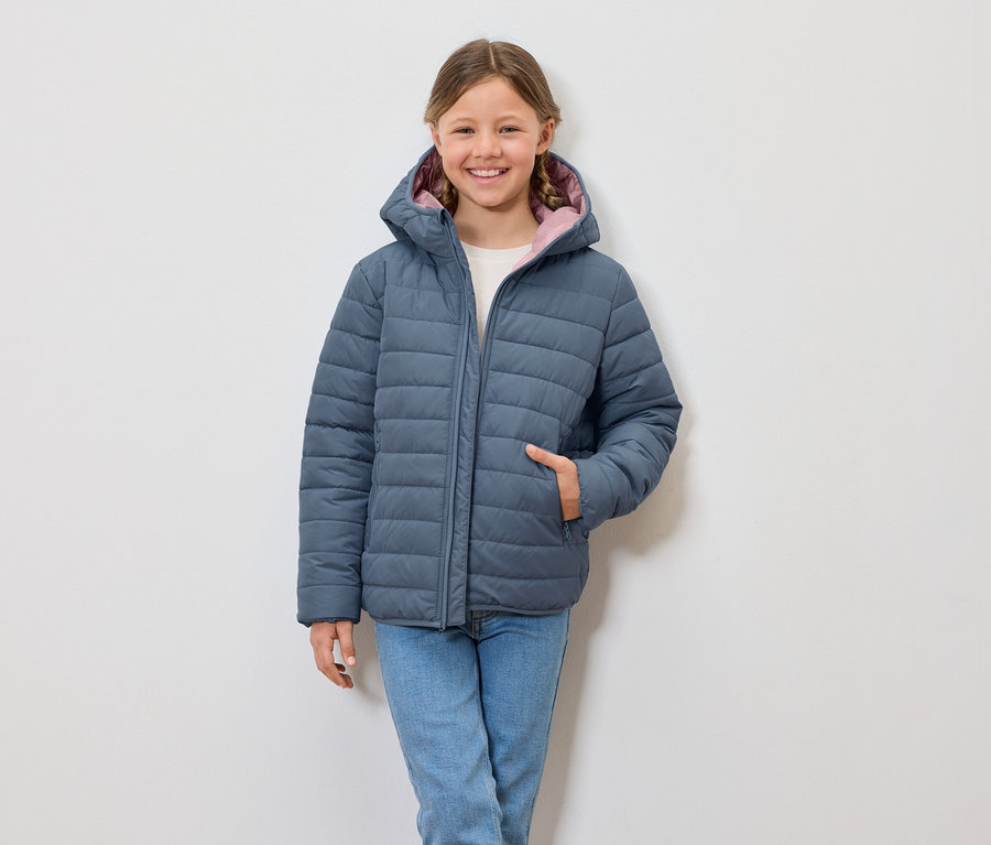 Lächelndes Mädchen trägt eine blaue Steppjacke mit Kapuze und Jeans.