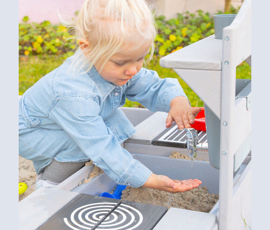 Blondes Mädchen spielt mit Wasser an roba Matschküche zum Hängen.