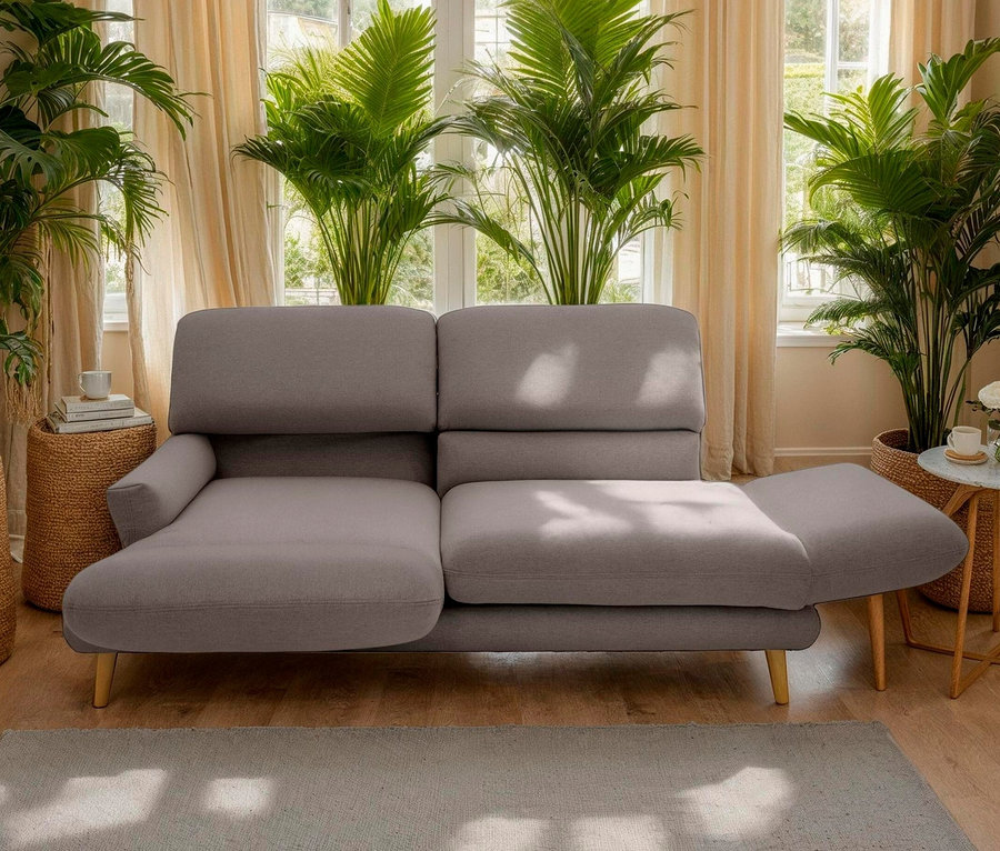 Wohnzimmer mit einem taupefarbenen DOMO 2-Sitzer-Sofa »FuAR«, drehbar, vor einem Fenster und Zimmerpflanzen.