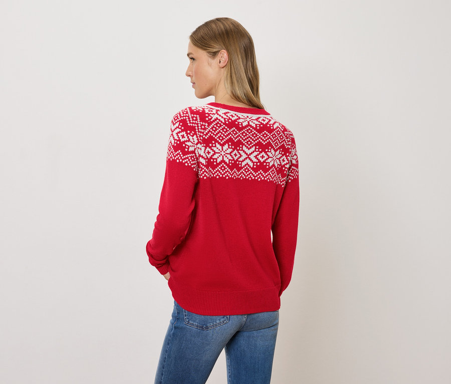 Frau blickt über die Schulter und trägt einen roten Pullover mit Norwegermuster und Jeans.