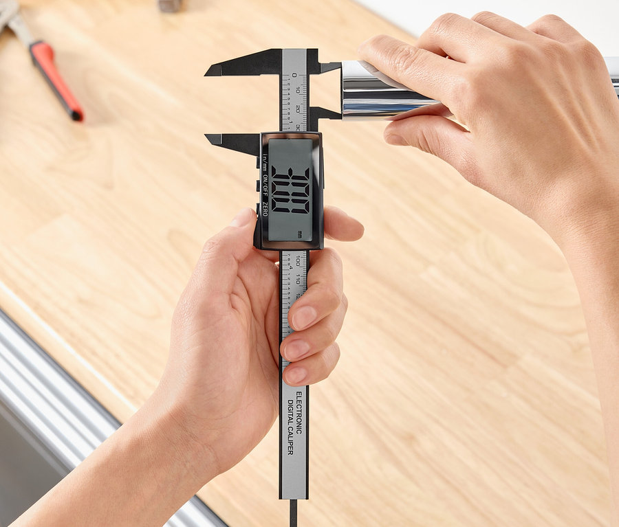 Eine Person misst den Durchmesser eines Metallrohrs mit einem digitalen Messschieber.