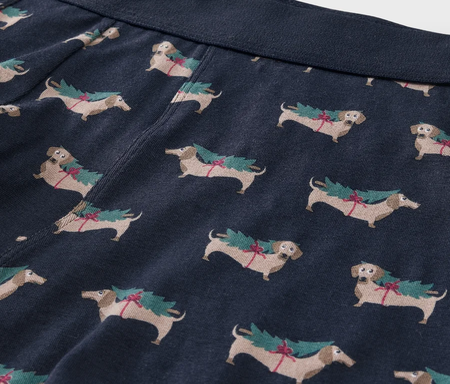 Detailansicht von blauen Boxershorts mit Dackel-Print, die Weihnachtsbäume tragen.