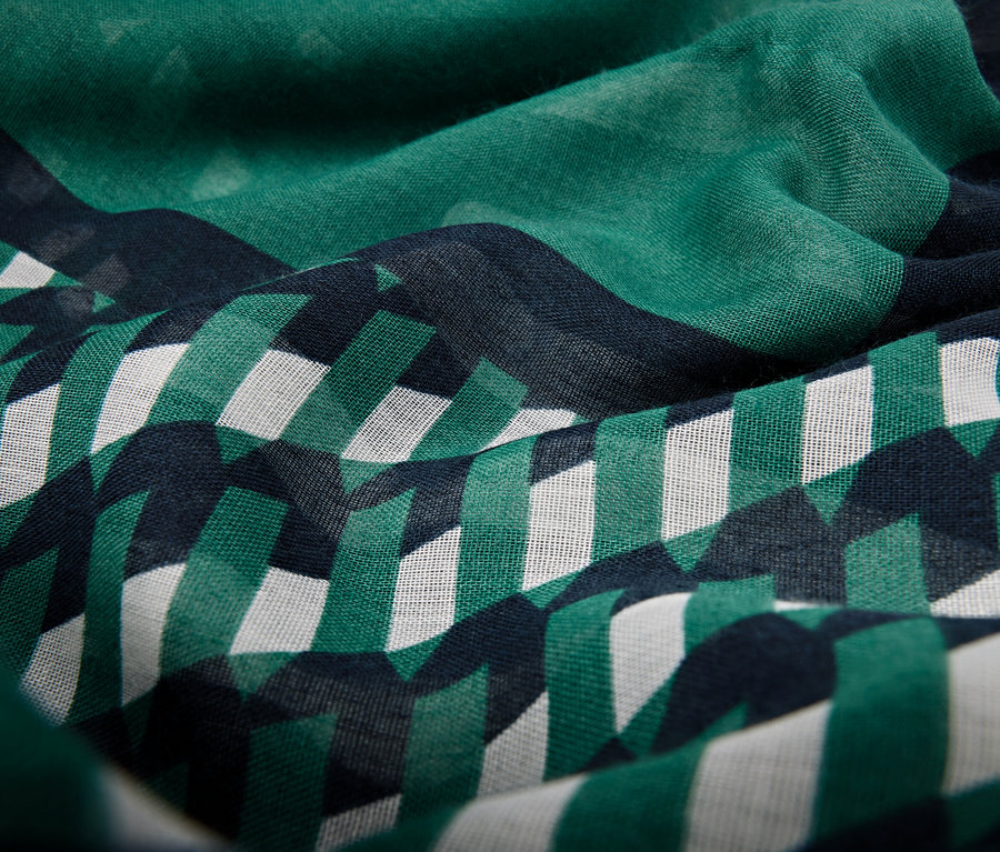 Nahaufnahme eines Stoffes mit einem Muster aus grünen und weißen geometrischen Formen auf dunkelblauem Grund.