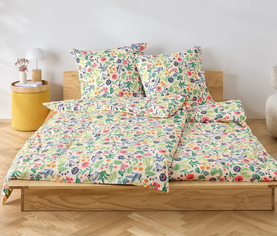 Blumige Jersey-Bettwäsche liegt auf einem Holzbett.