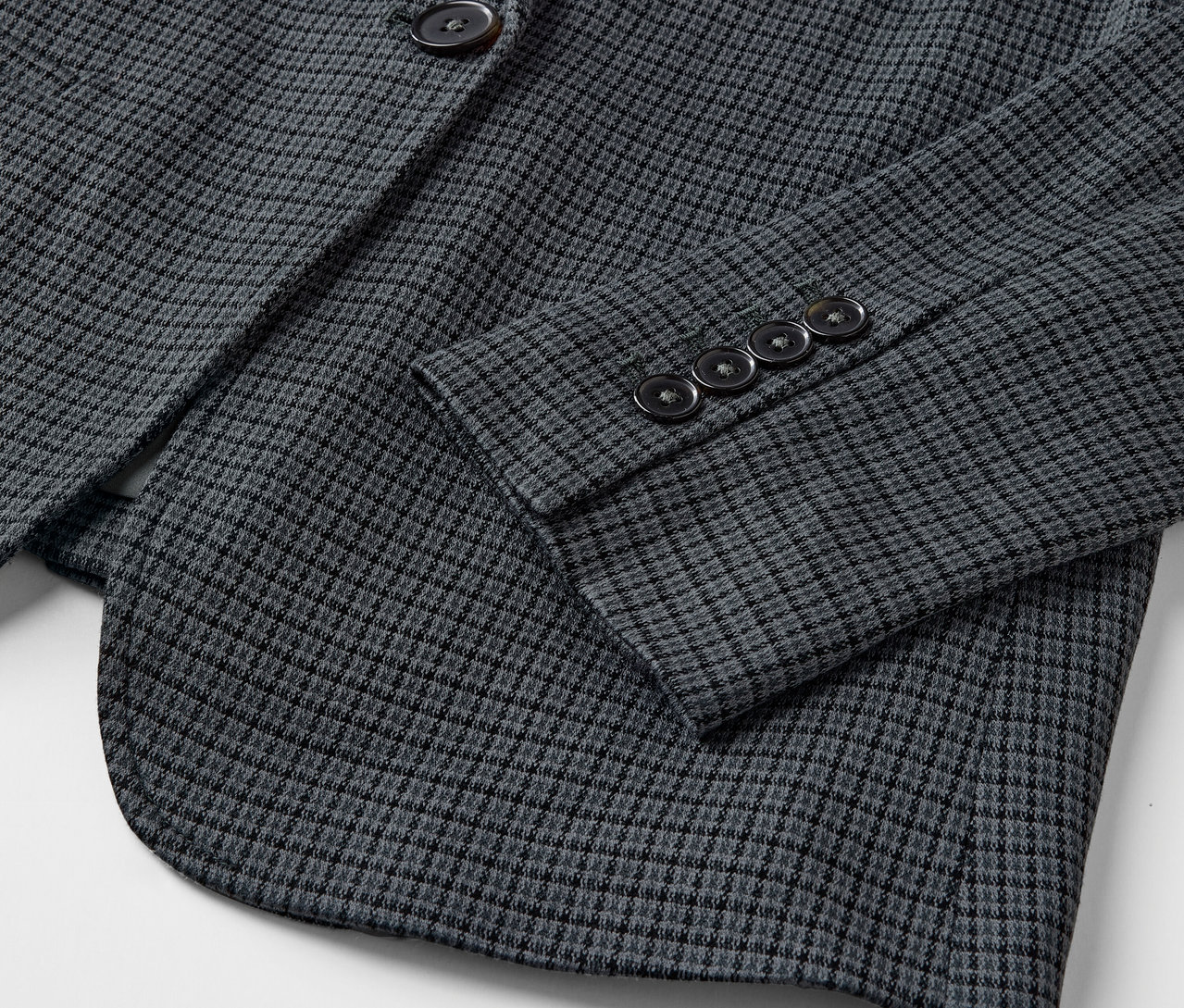 Detailaufnahme eines grauen Blazers mit kleinem Muster und Knöpfen am Ärmel.