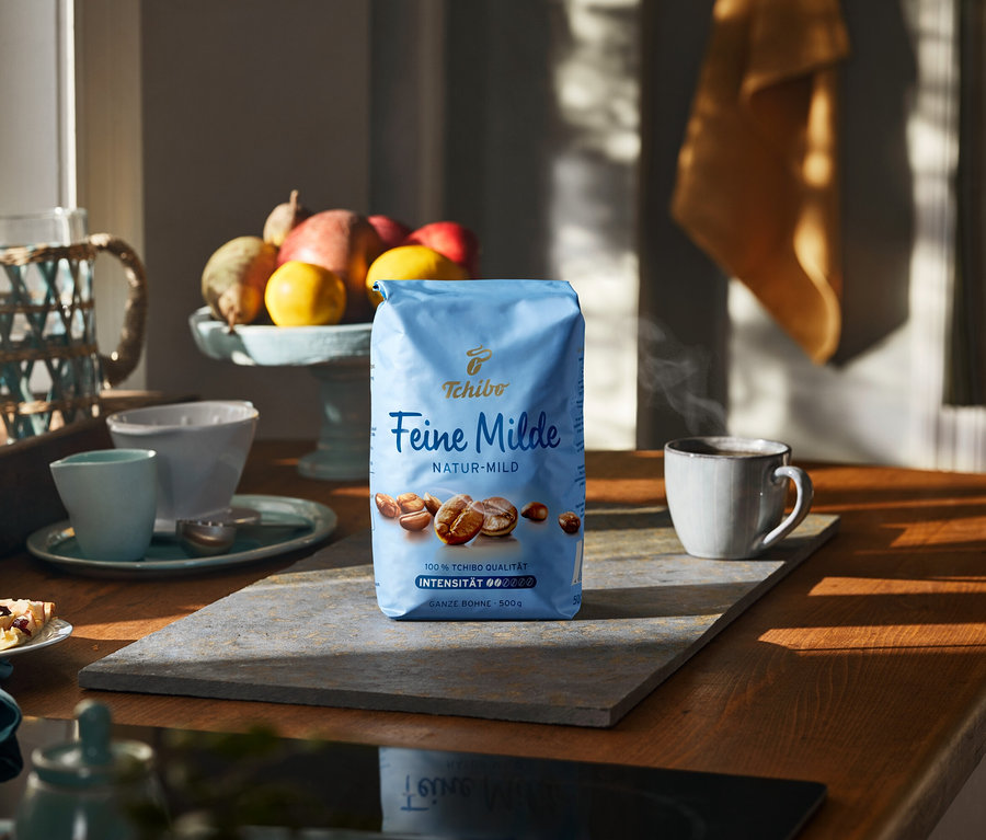 Eine 500-g-Packung Feine Milde Kaffee auf einer Steinplatte neben einer Tasse und Früchten.