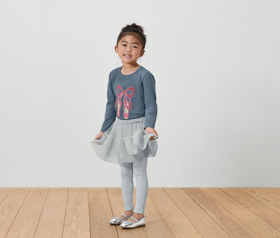 Mädchen im grauen Ballett-Outfit mit T-Shirt, Rock und Leggings.
