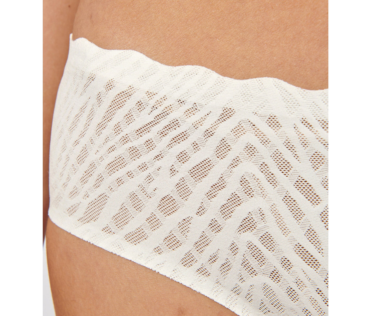 Nahaufnahme einer Hüfte, die einen seidenweißen sloggi ZERO Feel Bliss Hipster mit perforiertem Zickzack-Spitzenmuster und gewelltem oberen Rand trägt.