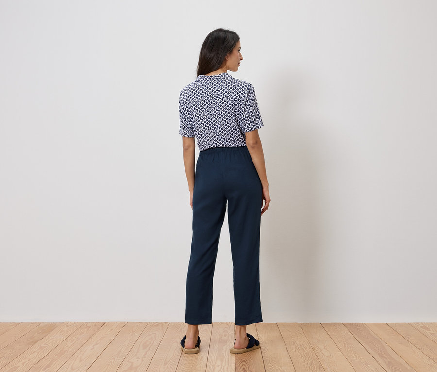 Eine Frau steht mit dem Rücken zur Kamera, trägt ein blau-weißes Oberteil und eine marineblaue Hose.