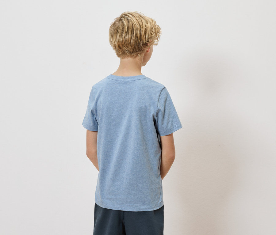 Rückansicht eines Kindes mit blonden, lockigen Haaren, das ein hellblaues T-Shirt und dunkelblaue Shorts vor einem weißen Hintergrund trägt.