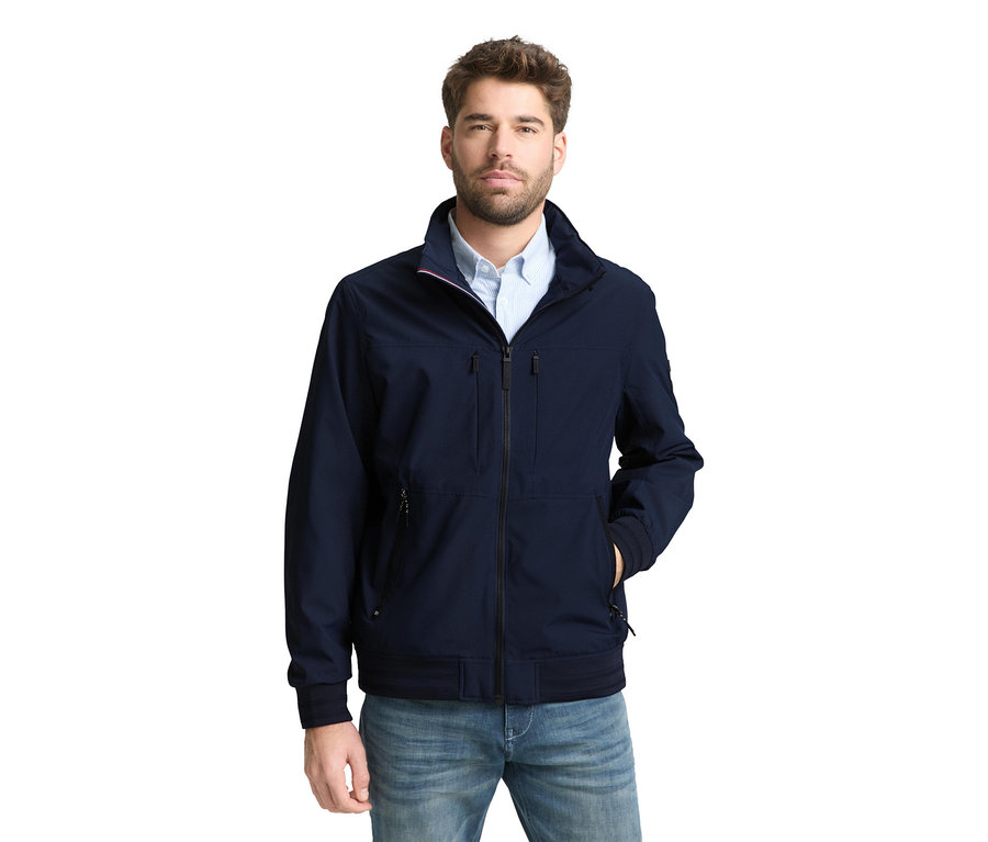 Mann mit Tom Tailor Blouson-Jacke in Sky Captain Blue und Jeans, eine Hand in der Tasche.