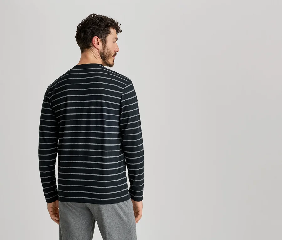 Mann von hinten, trägt ein schwarz-gestreiftes Langarmshirt und graue Hose vor einem hellen Hintergrund.