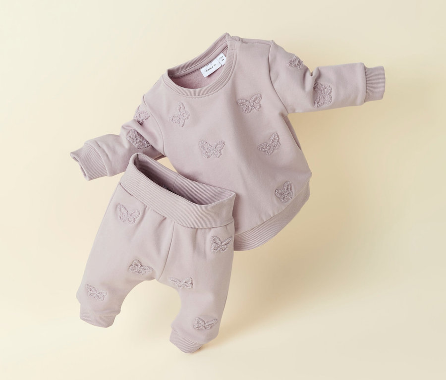 Baby-Sweatshirt von NAME IT und passende Hose in Lila mit Schmetterlingsmuster liegen auf beigem Grund.