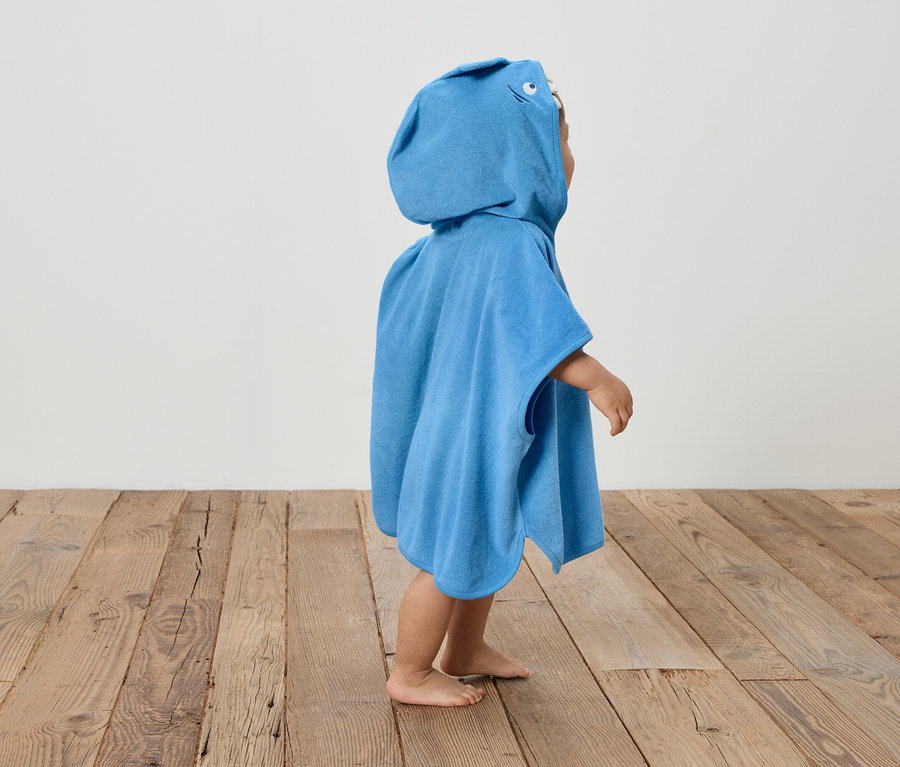 Ein Kind steht barfuß auf einem Holzboden und trägt einen blauen Kapuzenponcho.