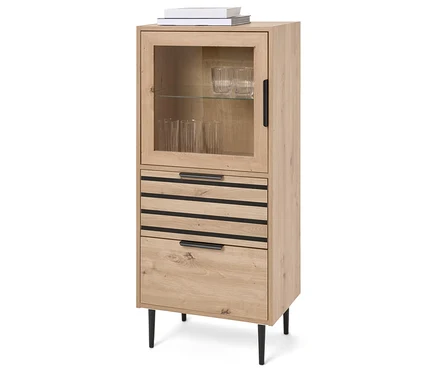 Ein hellbrauner Holzschrank mit einer Glastür oben und drei Schubladen darunter, der auf vier schwarzen Beinen steht. Auf dem Schrank liegen zwei Bücher.
