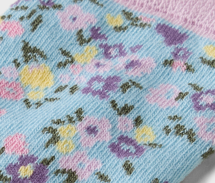 Nahaufnahme einer hellblauen Socke mit einem Blumenmuster in Gelb, Lila und Rosa.