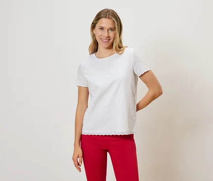 Frau mit blonden Haaren trägt ein weißes Lochstickerei-T-Shirt und eine rote Hose.