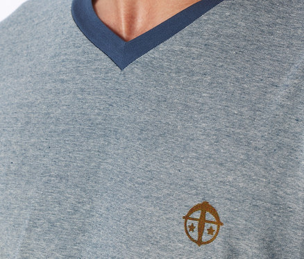 Nahaufnahme eines hellblauen V-Ausschnitt-T-Shirts mit dünnen Querstreifen und dunkelblauem Besatz, mit einem goldbraunen gestickten Logo auf der linken Brust.