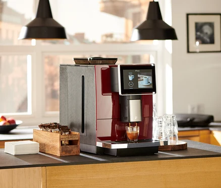 Roter »Tchibo Office« Kaffeevollautomat bereitet Kaffee in ein Glas auf einer Küchentheke zu.