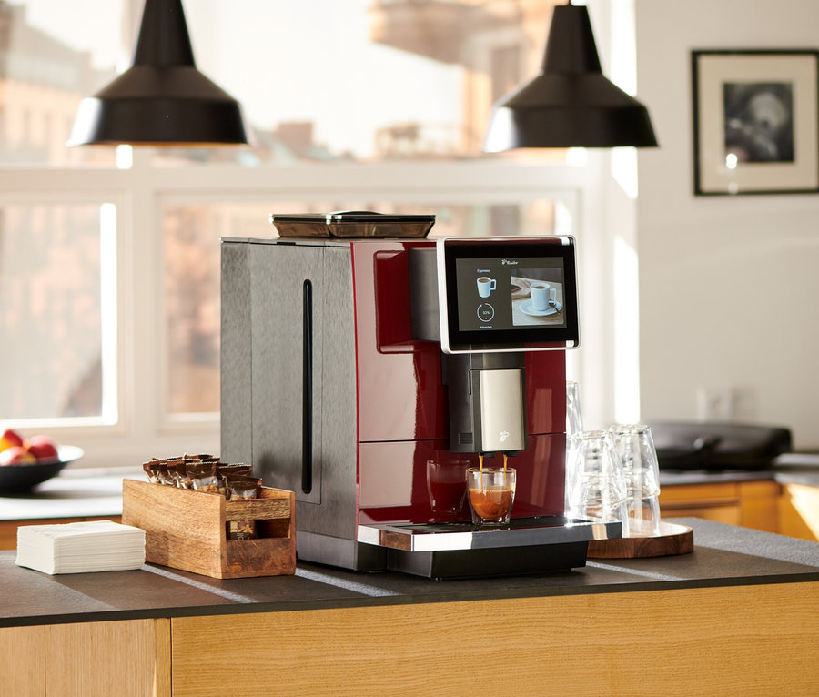 Roter »Tchibo Office« Kaffeevollautomat bereitet Kaffee in ein Glas auf einer Küchentheke zu.