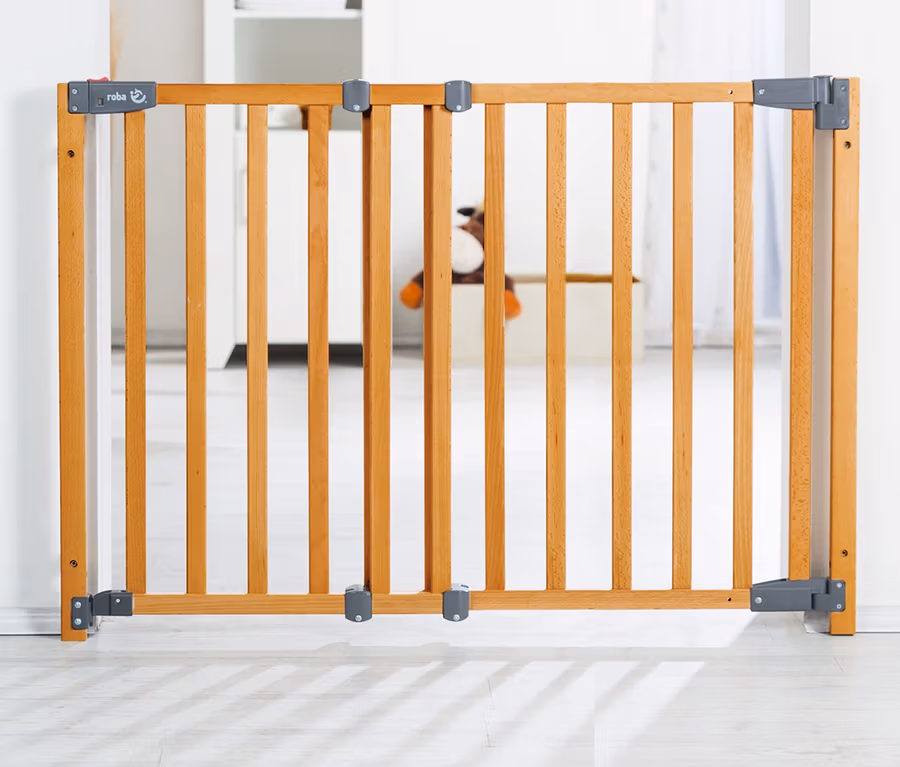 Ein hellbraunes roba Türschutzgitter »Safety Up« aus Holz mit vertikalen Latten und grauen Beschlägen ist in einem weißen Türrahmen installiert.