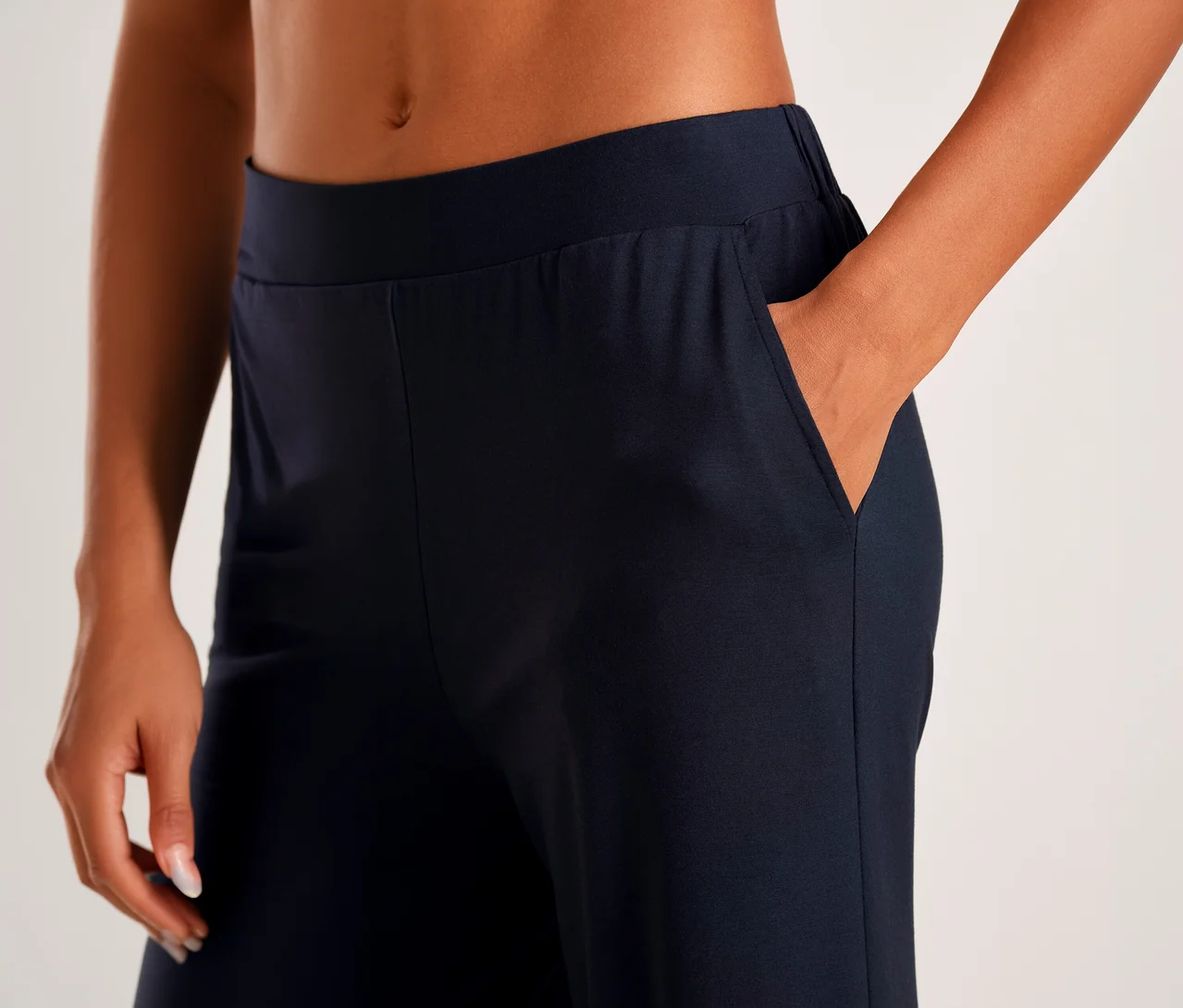 Nahaufnahme einer Person in marineblauen Hosen, eine Hand steckt in der Tasche, die andere ruht an der Seite. Der nackte Bauch ist sichtbar.