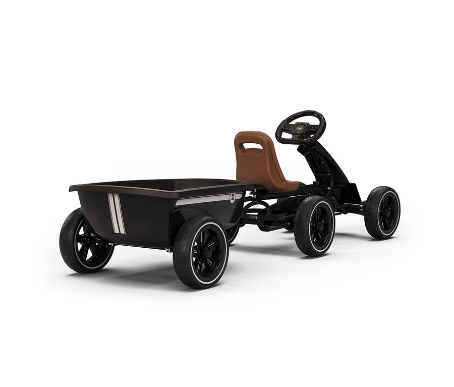 Ein schwarzes Tret-Gokart mit braunem Sitz und schwarzem Lenkrad, das einen schwarzen, rechteckigen Anhänger mit weißen Streifen zieht, alles auf weißem Hintergrund.